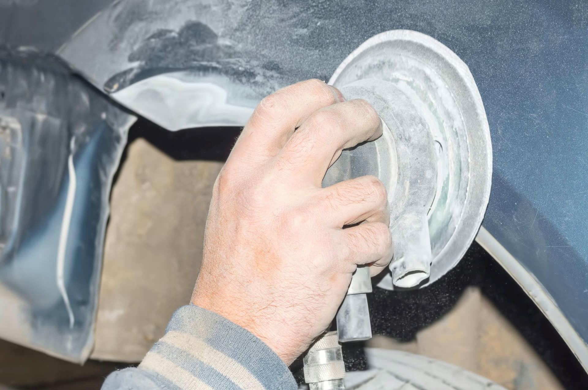 Hands sanding a damaged car panel with a rotary sander