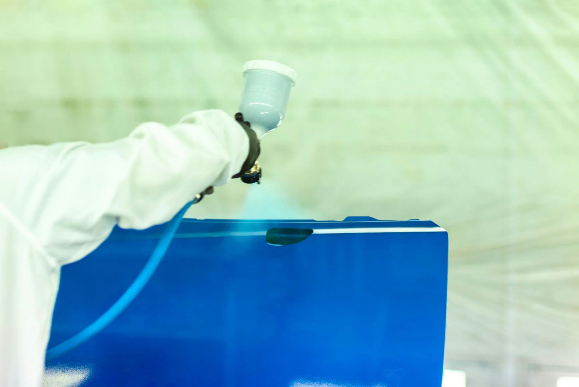 Painter applying base coat to a blue panel inside the spray booth