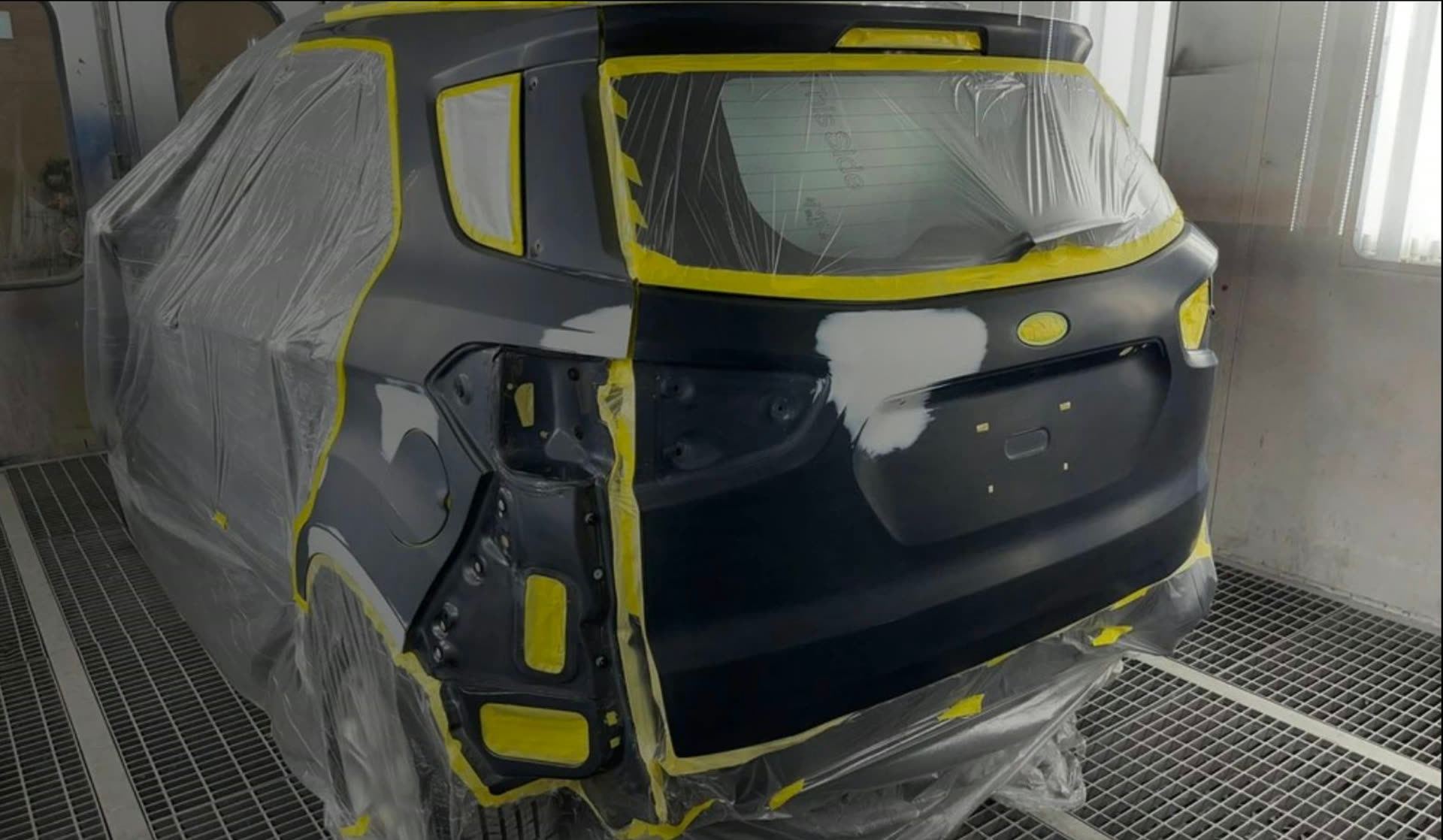 Black SUV with masking tape and protective sheeting in the spray booth